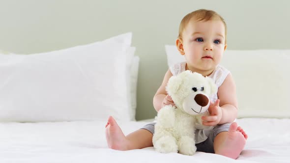 Cute baby girl playing with soft toy on bed