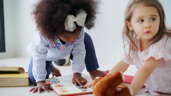 Cute Little Girls in Casual Clothing Reading Books and Playing Together in the Room