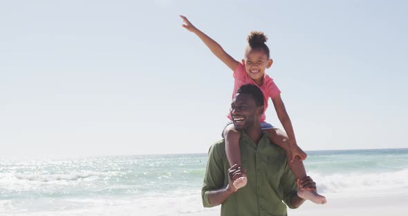 Smiling african american father carrying his daughter on sunny beach