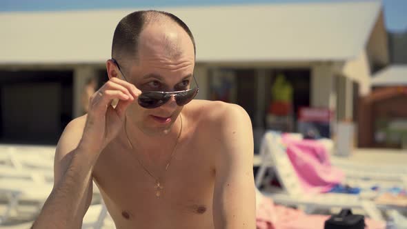 Closeup Italian Man Looks Cunningly at Girls He Sits on the Beach in Lounger Wearing Sunglasses