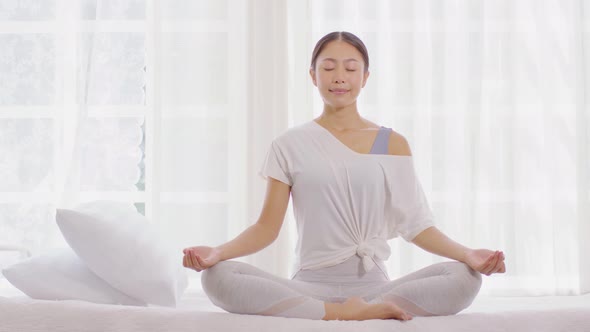 Calm of wellness Asian young woman sit on bed breathing with yoga lotus pose