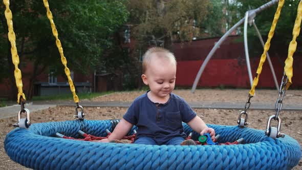Happy Little Boy Swings on a Round Swing