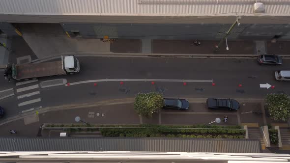 Top down view of a small street with cars, truck, and people crossing the road from the zebra cross.