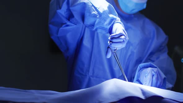 Mid section of surgeon wearing protective clothing holding scissors in operating theatre