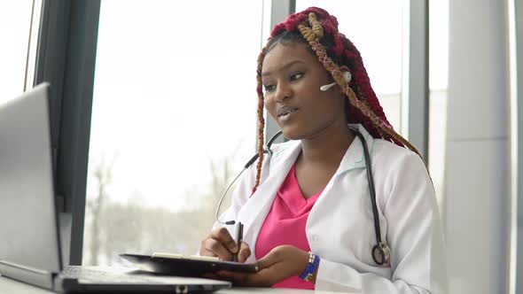 Young African American Woman Doctor with Red Hair Having Chat or Consultation on Laptop