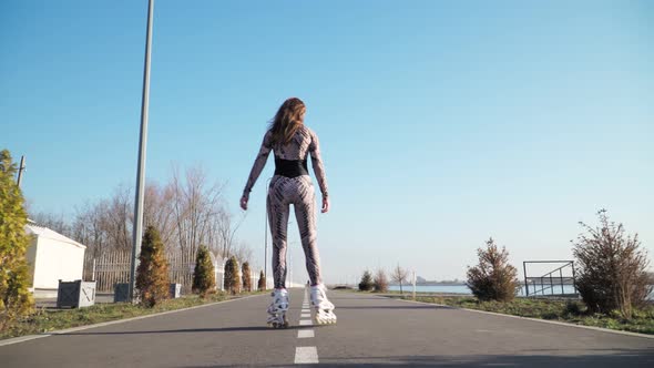 Athletic Slim Rides Girl Roller Skating Along the Path on the Background of a Beautiful Lake. 