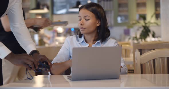Afro Businesswoman Paying with Credit Card Sitting at Table with Laptop in Cafe