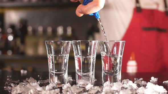 Close-up Bartender Pouring Some Drink From Bottle Into Shot Glasses on Wooden Counter