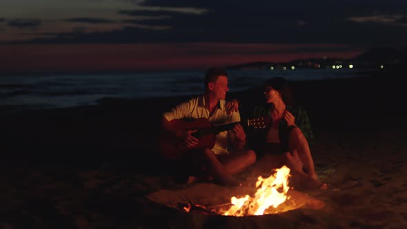 Couple sitting around campfire on beach