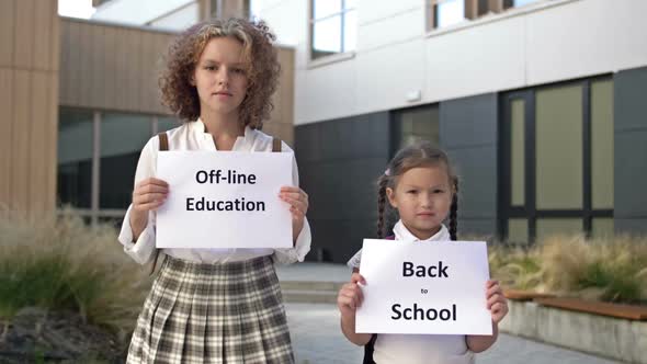 Two Schoolgirls with Placards are Standing in Front of the School Building