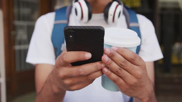 Midsection of mixed race man drinking coffee and using smartphone in the street