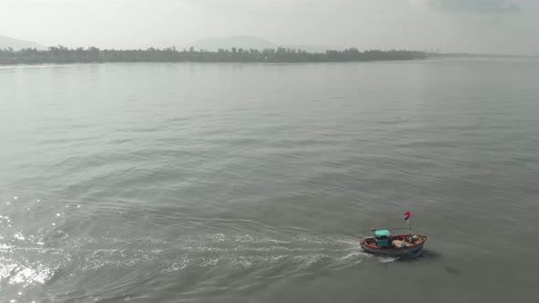 high profile follow Drone shot of small colourful Indian fishing boat going out to sea looking towar