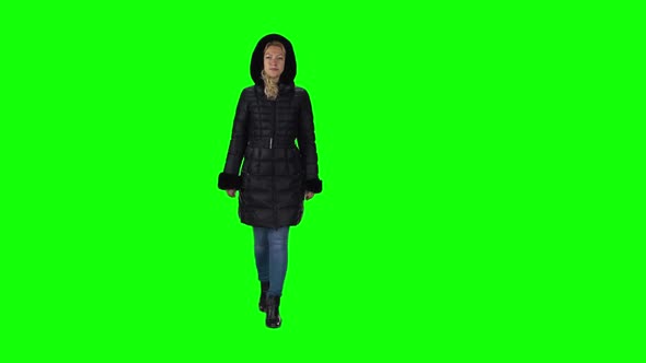 Blonde Girl in a Black Winter Coat with Hood, Jeans and Boots Going Against a Green Screen. Slow