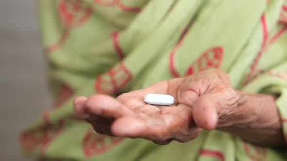 s Single Medical Pill on Palm of Senior Women Hand