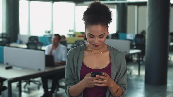 Young African Woman in Modern Office Business Woman Uses the Smartphone and Smiling Positive