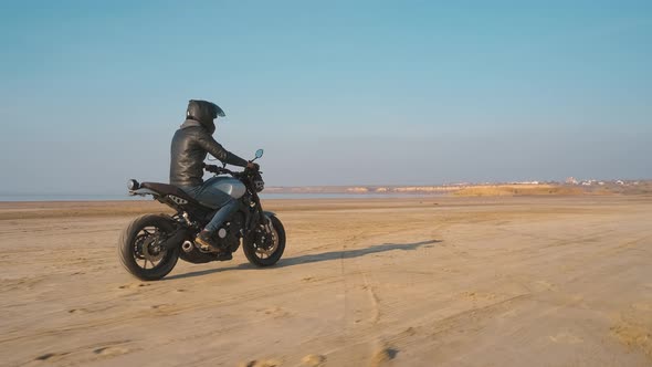 Motorcyclist Driving His Customized Fast Motorbike on the Dirt Road in Desert Around Sea or Lake