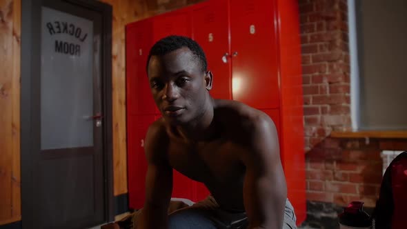 Africanamerican Athletic Young Man Sitting in Locker Room and Looking in the Camera