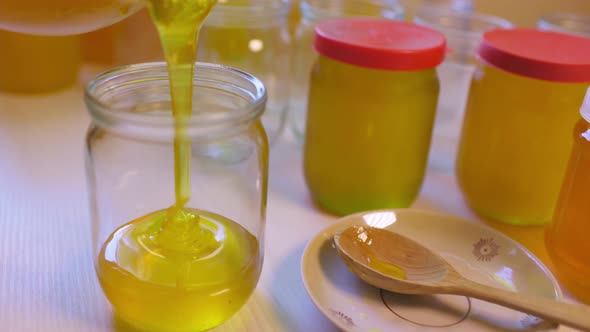 Woman Pours Honey Into Transparent Jars on a White Table