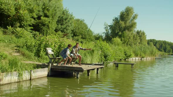 Excited Teenage Fisherman and Dad with Fishing Rod Catching Fish on Lake