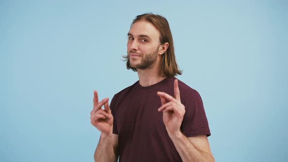 Young Handsome Guy is Snapping His Fingers Pointing at you and Smiling Posing Against Blue Studio