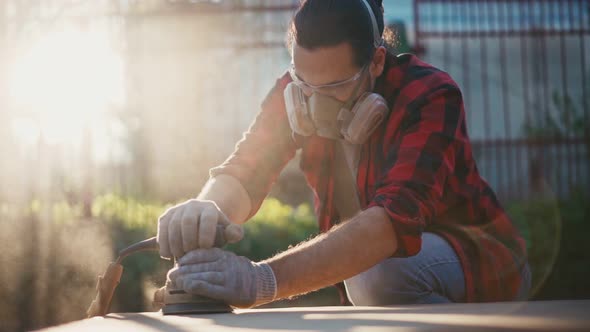 A Young Man in a Construction Respirator Grinds a Parquet Board with a Sander