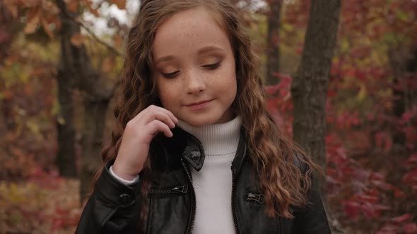 Portrait of a Little Girl with Long Curly Hair and Freckles in a Park in Autumn.