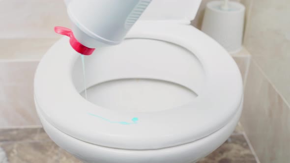 Liquid Soap of a Bright Color is Poured From a Plastic Bottle on the Rim of the Toilet