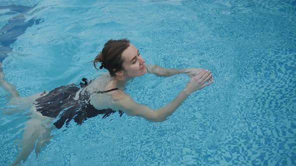 Cute Girl in a Black Swimsuit Swims in the Pool