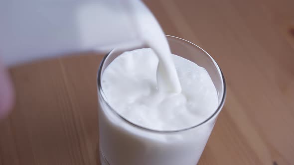 Pouring Fresh Milk Into a Glass Standing on a Wooden Table