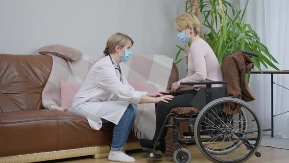 Wide Shot of Professional Doctor in Covid19 Face Mask Talking with Disabled Patient Putting Hands on