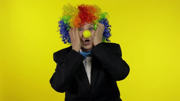 Senior Old Woman Clown in Colorful Wig Looks Surprised Shocked. Amazement