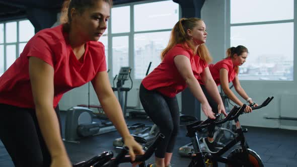 Group of Smiling Friends Women Class Exercising Training Spinning on Stationary Bike at Modern Gym