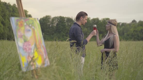 Romantic Creative Couple Drinking Wine and Talking with Blurred Artwork Standing at Front