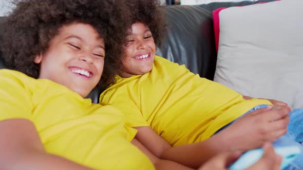 Twin brothers lying on couch watching video on smartphone