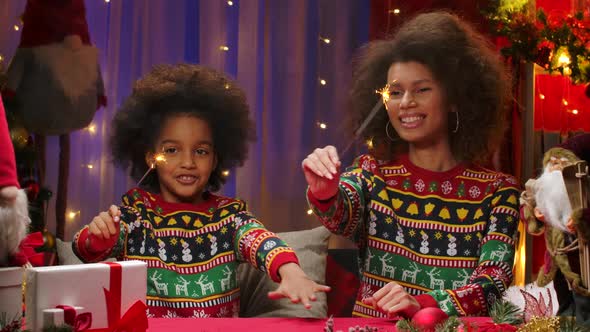 African American Mom and Little Daughter in Bright Holiday Sweaters Light Sparklers and Paint a