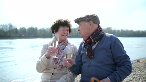 Senior couple in love kissing and drinking champagne at the riverside
