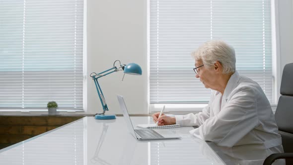 Skilled mature lady doctor writes in paper notebook