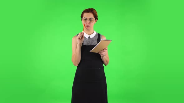 Funny Girl in Round Glasses Is Thinking, Then Writing with Pencil in Notebook. Green Screen