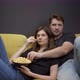 Attractive Young Couple Sitting on Sofa with Popcorn Watching Movie on TV - VideoHive Item for Sale