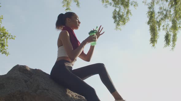 Athlete Sits on Rock Drinking Water After Training