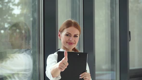 Happy Young Caucasian Woman Doctor Wearing White Medical Coat and Stethoscope with Notepad Looking