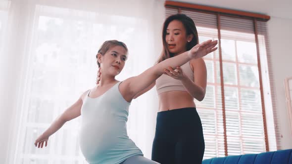 Pregnant woman doing yoga exercise with personal trainer at home.