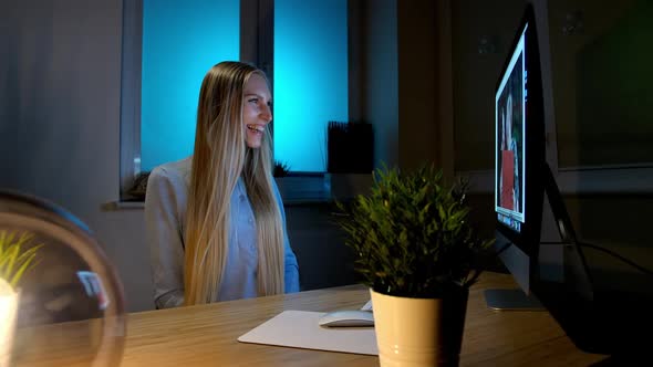 Smiling Woman Working on Computer at Night. Smiling Female in Checkered Shirt Sitting at Lit By