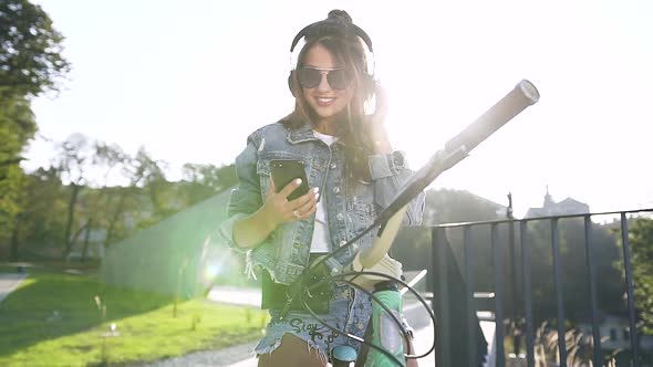 Young Woman in Sunglasses Dressed in Modern Denim Clothing Cycling while Listening to Music