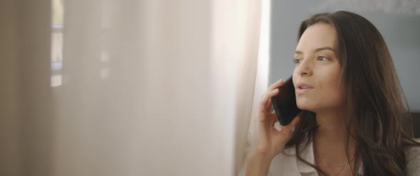 Close up of a woman talking to someone on the phone, near the window