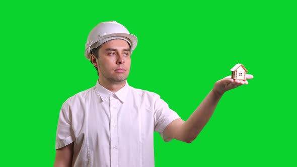 Young Male Smiling Engineer in White Hardhat and Shirt Standing and Showing Hand Palm with Small