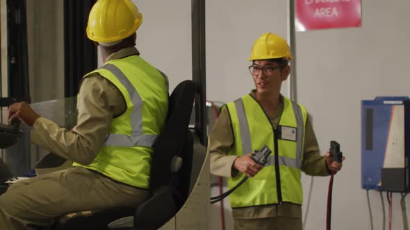 Diverse male workers wearing safety suits and sitting in turret truck in warehouse