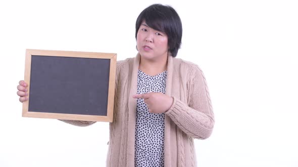 Stressed Overweight Asian Woman Holding Blackboard and Giving Thumbs Down for Winter