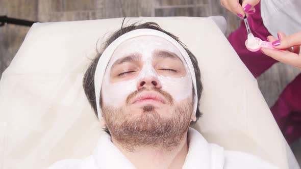 Concept of Spa for Men. A Young Man Is Applied a Cosmetic Mask on the Face in a Beauty Salon