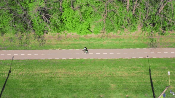 Two Cyclists Ride on an Asphalt Bike Path in the Park in the Spring